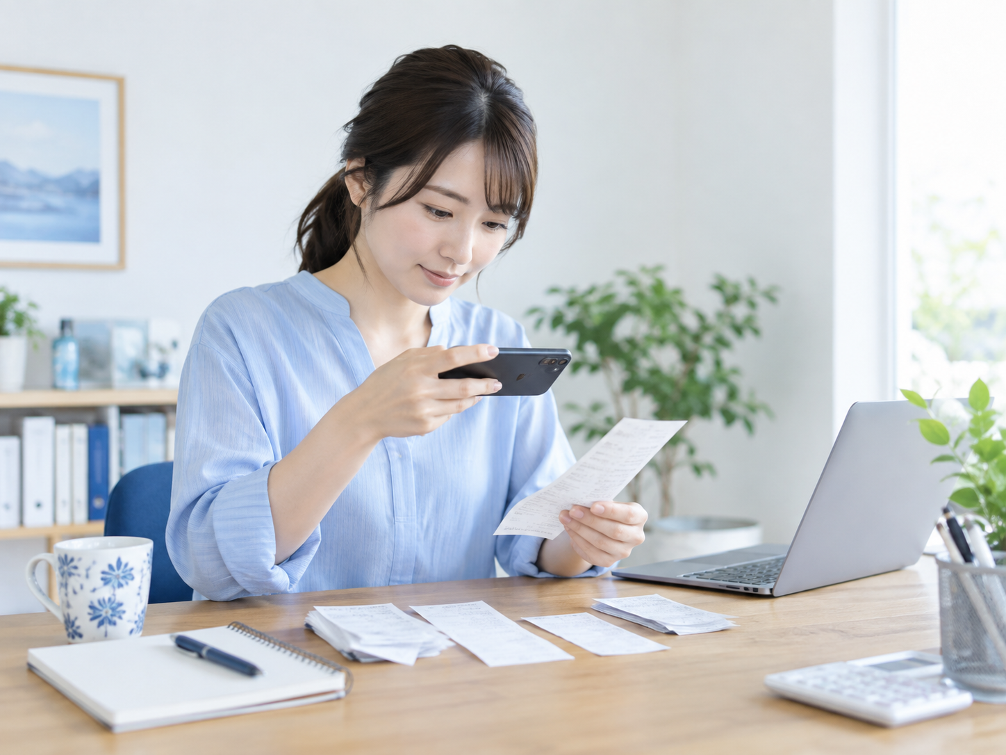 自宅の机でレシートをスマートフォンで撮影し、その場で保存している個人事業主